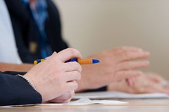 Image of someone holding a pen with paper on the desk